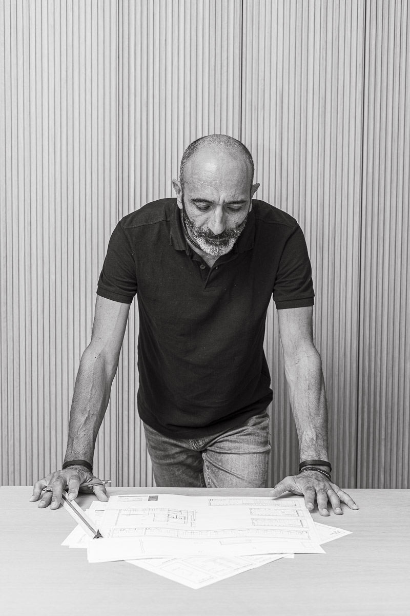 Foto en blanco y negro de Manuel Jamardo, diseñador de interiores en Santiago de Compostela. Está apoyado sobre una mes mirando unos planos en papel